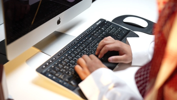 لقطة على يدين رجل يظهر لوحة مفاتيح جهاز كمبيوتر في مكتب، لقطة قريبة.