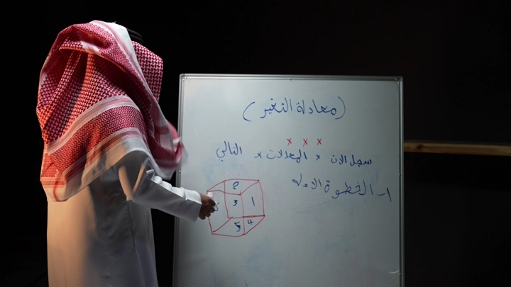 رجل سعودي يكتب على سبورة في غرفة دراسية، لقطة جانبية.