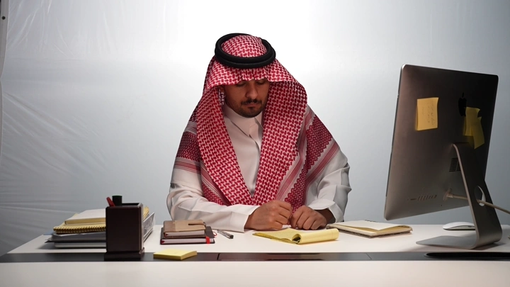 رجل سعودي يعمل في مكتب حديث، لقطة داخلية.