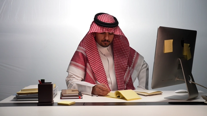 رجل سعودي يعمل على مكتبه، لقطة داخلية.