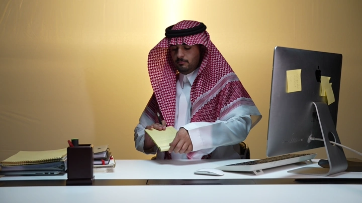 رجل سعودي يرتب المكتب مع كمبيوتر، لقطة داخلية.