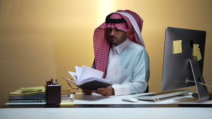 رجل سعودي يقرأ في مكتبه، تصوير داخلي.