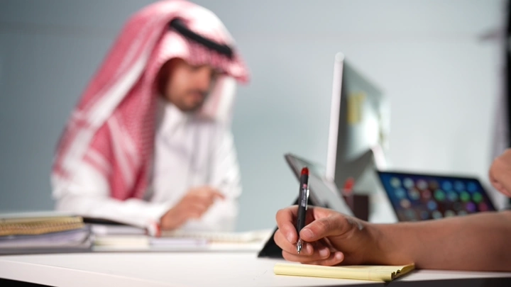 رجل سعودي يكتب في مكتب حديث، لقطة قريبة.