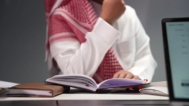 رجل سعودي يقرأ كتابًا في مكتب، لقطة مقربة.