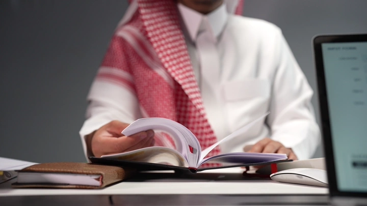 رجل سعودي يقرأ كتابًا في مكتب، لقطة مقربة.