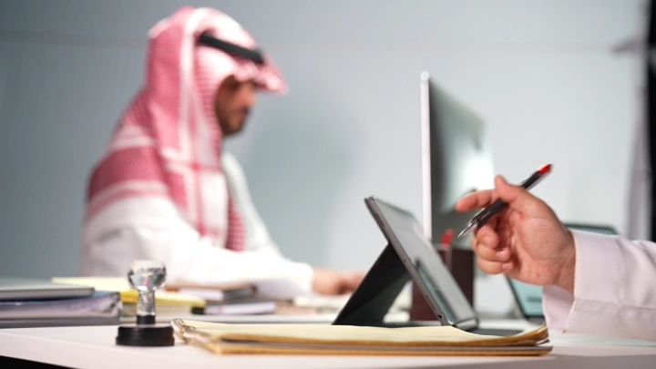 رجل سعودي يكتب في مكتب حديث، لقطة داخلية.