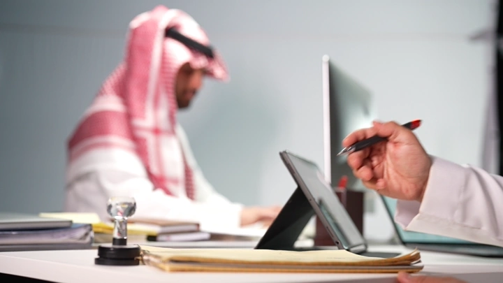 رجل سعودي يكتب في مكتب حديث، لقطة قريبة.