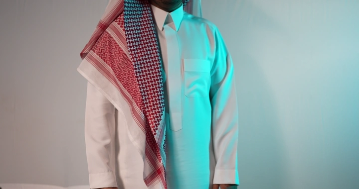 رجل يصفق و  يرتدي الثوب والغترة يقف في استوديو بإضاءة زرقاء.