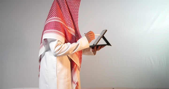 رجل سعودي يرتدي ثوب وغترة يستخدم جهاز ايباد، لقطة جانبية.