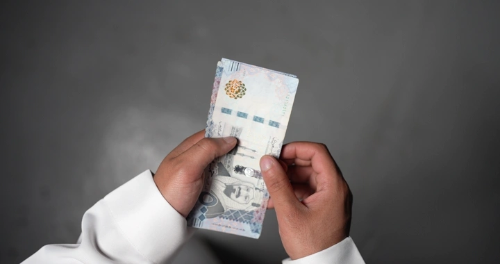 رجل سعودي يعد النقود بيديه، لقطة من الأعلى.