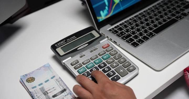 رجل يحسب النقود بجانب حاسوب محمول وآلة حاسبة، لقطة مقربة.