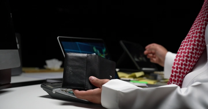 رجل سعودي يحمل محفظة ويقدم النقود لشخص في مكتب، لقطة مقربة.