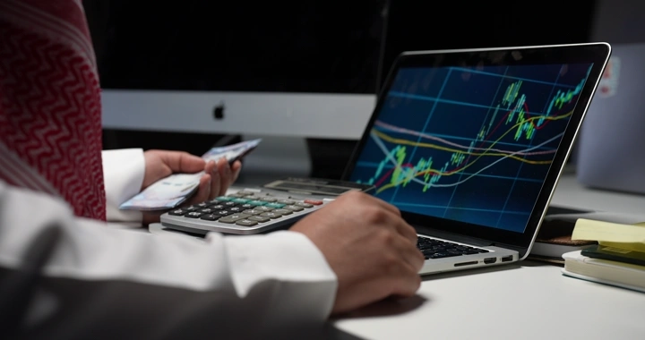 رجل سعودي يحسب المال أمام حاسوب محمول، لقطة داخلية.