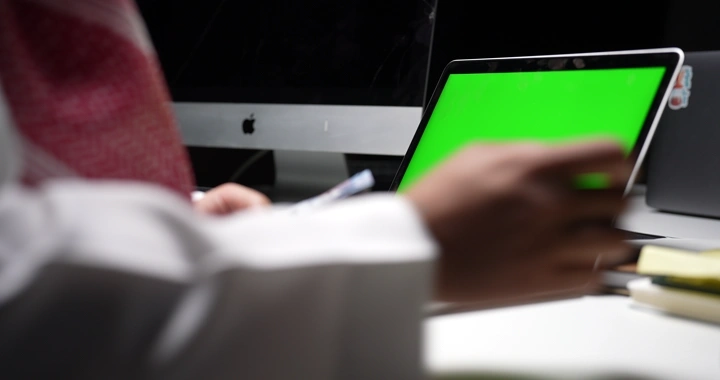 رجل سعودي يعمل على كمبيوتر محمول بشاشة كروما خضراء، لقطة داخلية.