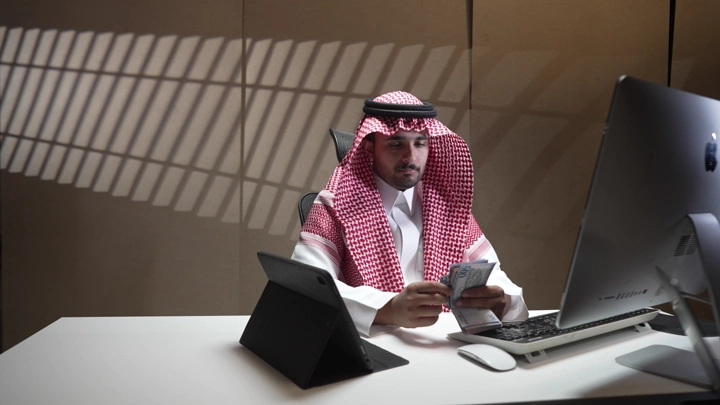 رجل سعودي يعد المال في مكتب حديث، لقطة داخلية.