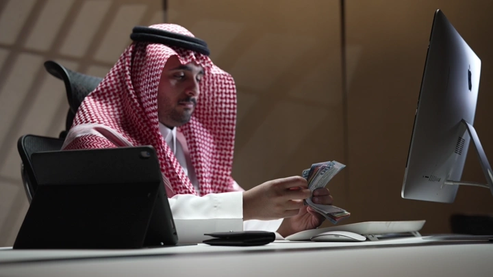 رجل سعودي يعد المال في مكتب حديث، لقطة داخلية.