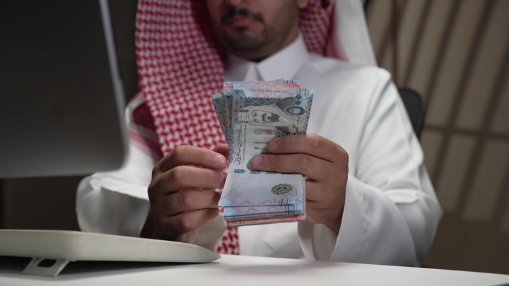 رجل سعودي يعد المال في مكتب، لقطة قريبة.