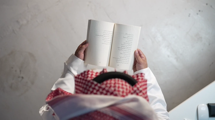 رجل سعودي يقرأ كتابًا في الداخل، لقطة من الأعلى.