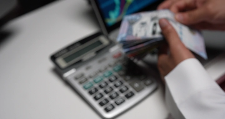 رجل يعد النقود بجانب آلة حاسبة على مكتب، لقطة مقربة.