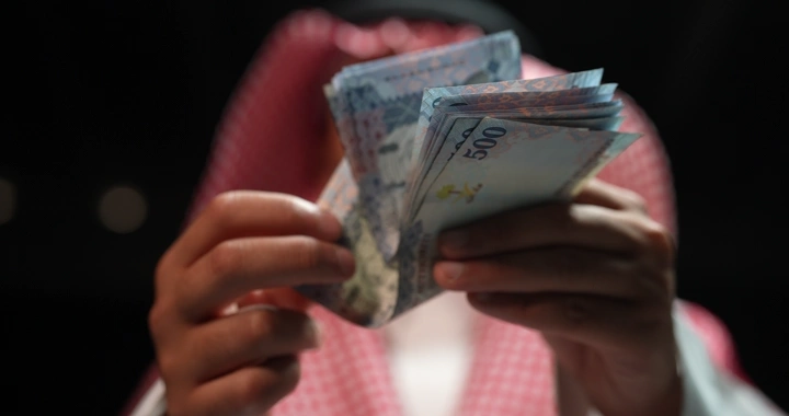 رجل سعودي يعد النقود في إضاءة خافتة، لقطة مقربة.