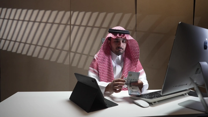 رجل سعودي يعد النقود في مكتب حديث، لقطة داخلية.