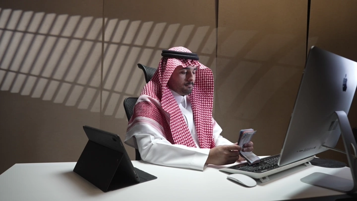 رجل سعودي يعد النقود في مكتب حديث، لقطة داخلية.