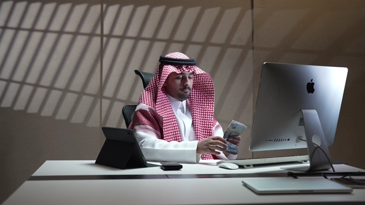 رجل سعودي يعد النقود في مكتب حديث، لقطة داخلية.