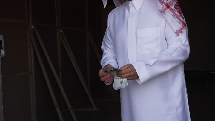 رجل سعودي يعد النقود في مكان داخلي، لقطة مقربة.