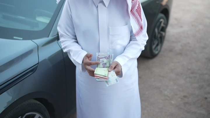 رجل سعودي يعد النقود بجانب سيارة، لقطة قريبة.