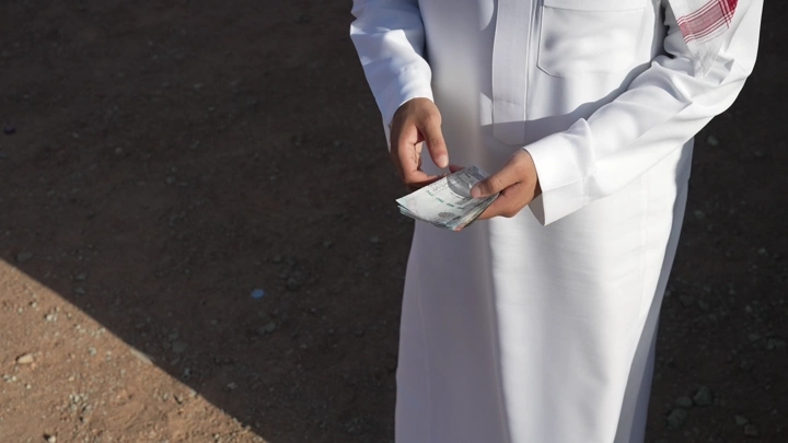 رجل يرتدي ثوبًا يعد المال في الخارج، لقطة قريبة.