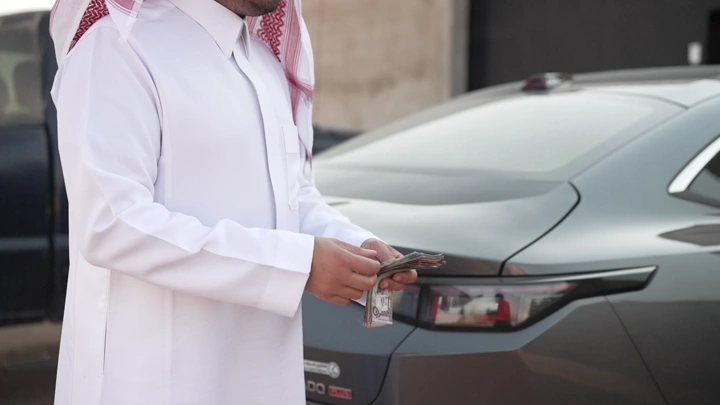 رجل سعودي يعد نقودًا بجانب سيارة، لقطة قريبة.