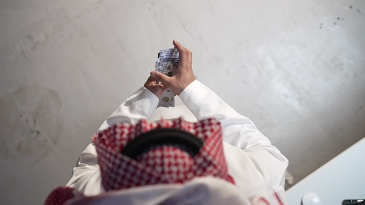 رجل سعودي يعد النقود في مكتب، لقطة من الأعلى.
