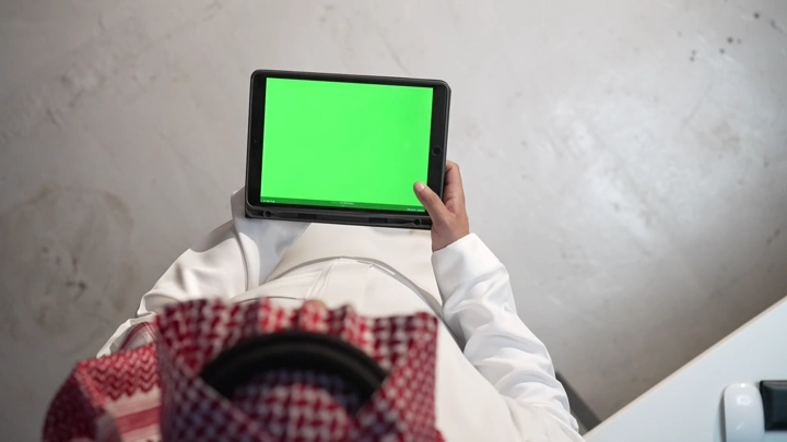 رجل سعودي يحمل جهاز لوحي بشاشة كروما خضراء، لقطة علوية.