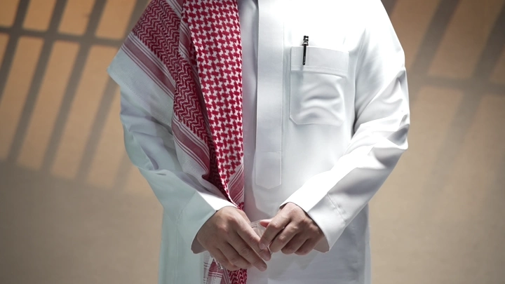 رجل يرش العطر و يرتدي ثوبًا وغترة في الداخل، لقطة قريبة.