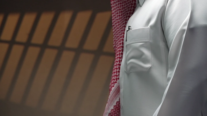 رجل يرش العطر و يرتدي ثوبًا تقليديًا في ضوء خافت، لقطة جانبية.