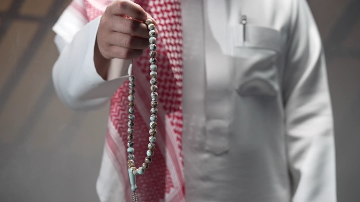 رجل يرتدي ثوبًا أبيض يحمل سبحة، لقطة قريبة.