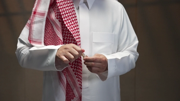 رجل يرتدي الثوب والشماغ يمسك بزجاجة دهن عود، لقطة مقربة.