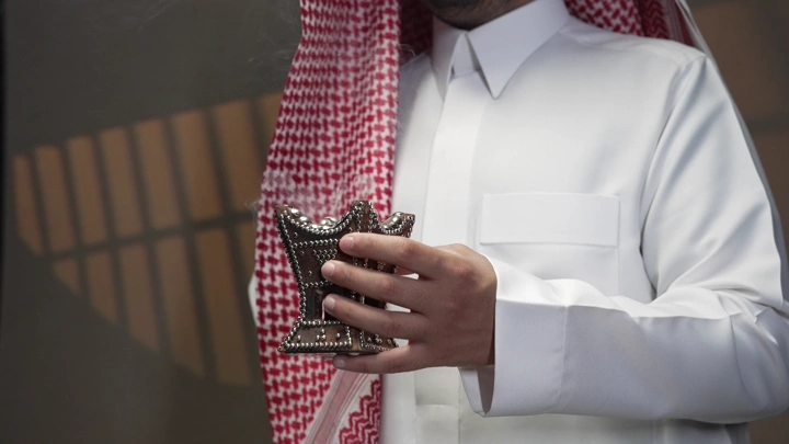 رجل سعودي يحمل مبخرة تقليدية، تصوير قريب في الداخل.