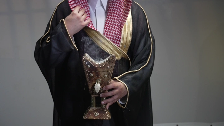 رجل سعودي يرتدي ثوباً تقليدياً يقدم البخور، لقطة قريبة.