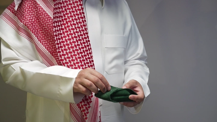 رجل يمسك ساعة و يرتدي ثوبًا وغترة ، لقطة مقربة.