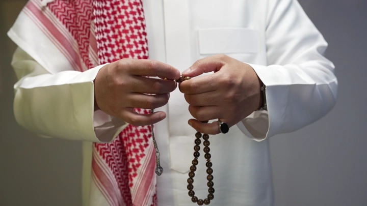 رجل يرتدي ثوبًا أبيض ويمسك مسبحة، لقطة قريبة.