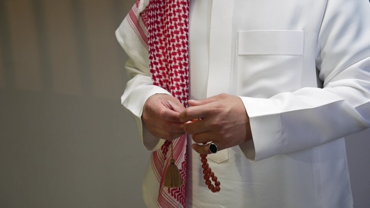 رجل يرتدي ثوبًا أبيض يمسك مسبحة، لقطة قريبة.