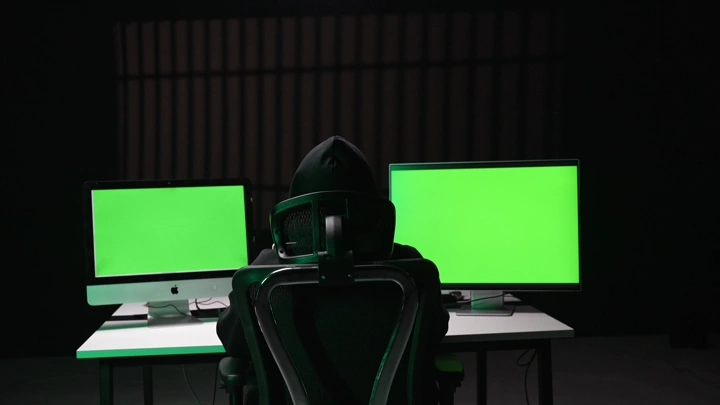 رجل جالس أمام شاشات كروما خضراء في غرفة مظلمة، لقطة من الخلف.