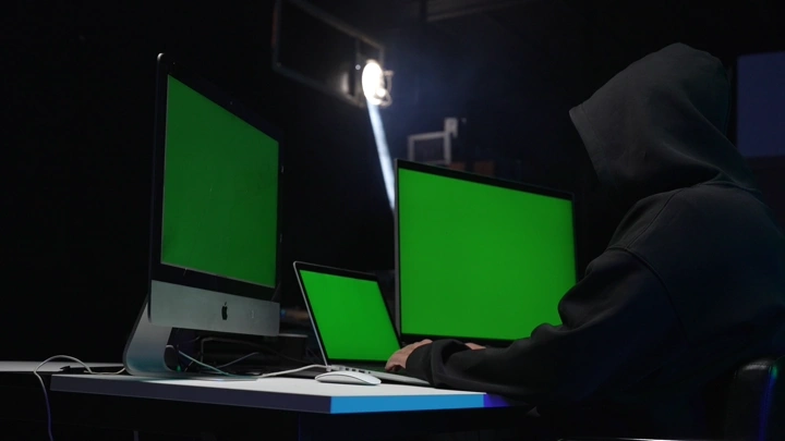شخص يرتدي سترة أمام شاشات كروما خضراء في غرفة مظلمة.