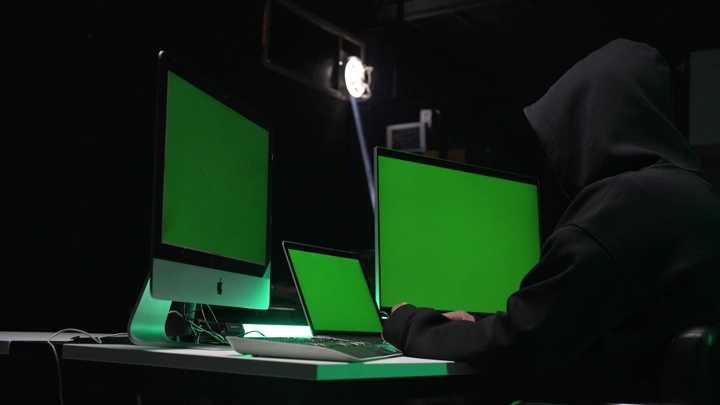 شخص يرتدي سترة أمام شاشات كروما خضراء في غرفة مظلمة، لقطة داخلية.