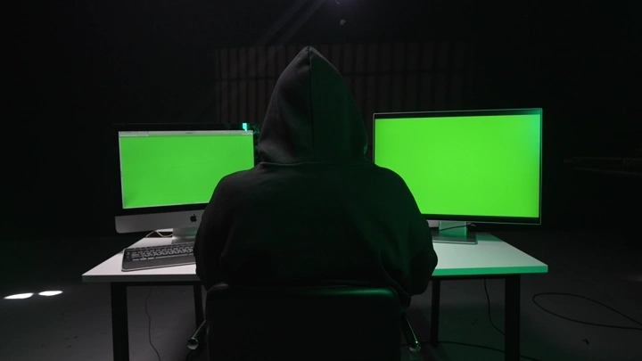 شخص جالس أمام شاشات كروما خضراء في غرفة مظلمة، لقطة من الخلف.
