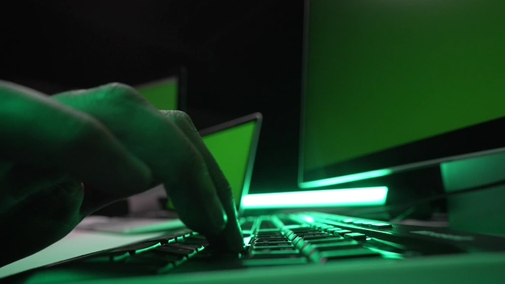 يد تكتب على لوحة مفاتيح بإضاءة خلفية خضراء، لقطة مقربة.