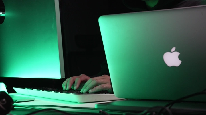 شخص يكتب على لوحة مفاتيح أمام شاشات خضراء، لقطة داخلية.