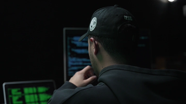 رجل يبرمج على شاشة في غرفة مظلمة، لقطة من الخلف.