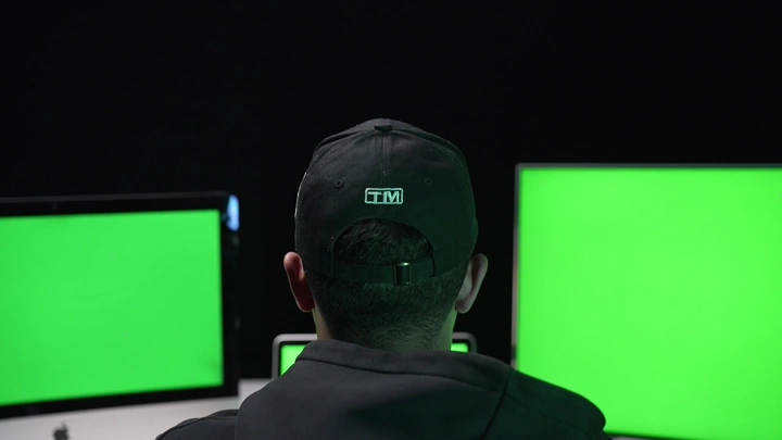 رجل يجلس أمام شاشات كروما خضراء في غرفة مظلمة، لقطة من الخلف.